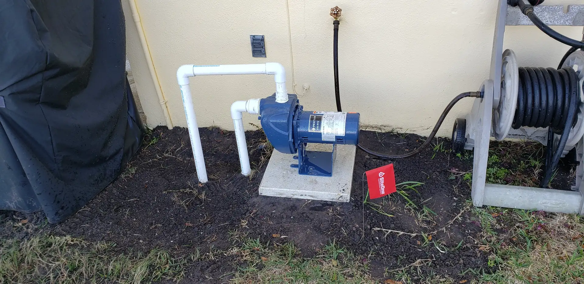 Newly installed irrigation pump with white PVC plumbing beside a home