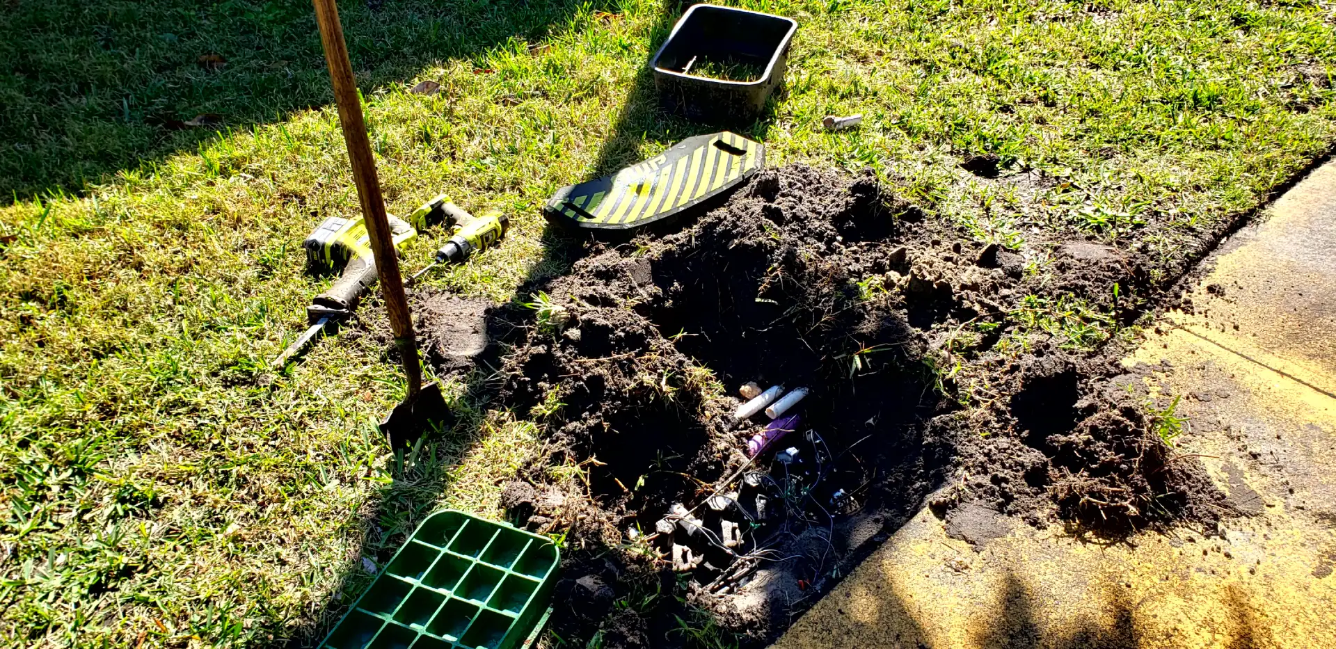 Sprinkler valve box dug out in a lawn for repair, tools beside it